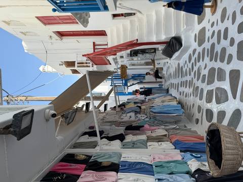 Narrow pedestrian alley in Mykonos lined with white buildings, colorful clothes shops and tourists.