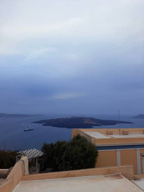 Overcast panoramic view of a volcanic island in the Santorini caldera with cruise ships below.