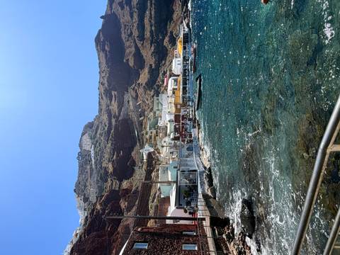 Seaside village with colorful houses built into steep volcanic cliffs beside sparkling blue water.
