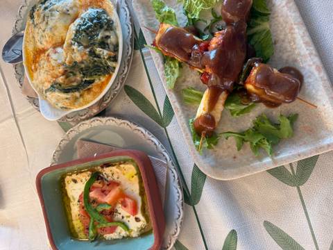 Close-up of traditional Greek dishes including baked feta, spinach gratin and meat in sauce on a rustic table.