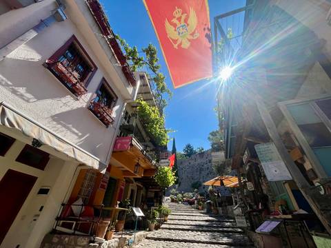 A sun-drenched alley lined with balconies, flags and cafés leads up stone steps between old buildings.