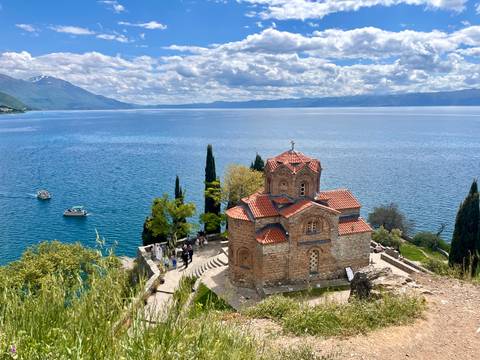 The lakeside Church of St. John at Kaneo perches on a rocky bluff above the shimmering blue water.