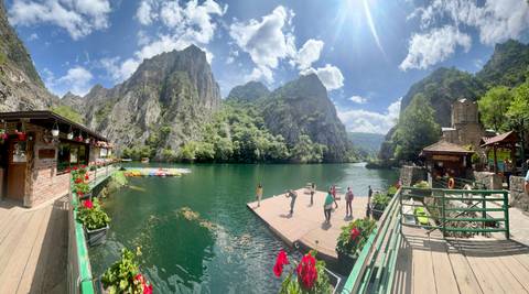 Visitors practise yoga on a dock in emerald Matka Canyon framed by soaring limestone cliffs and flowers.