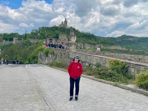 A traveller smiles on a cobbled road leading to the hilltop Tsarevets Fortress dotted with visitors.