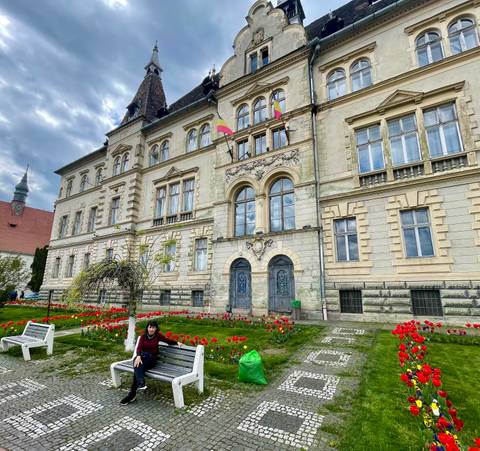 An ornate historic building fronted by red tulip beds is enjoyed by a seated visitor.
