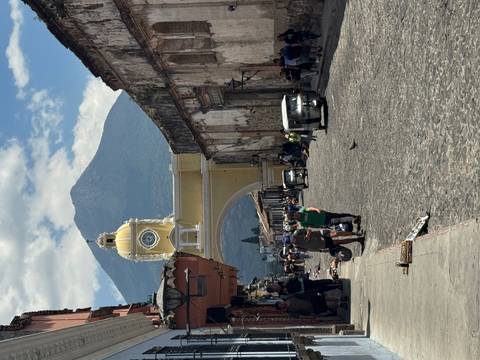 Crowds walk beneath Antigua’s yellow Santa Catalina Arch with towering Volcán de Agua beyond.