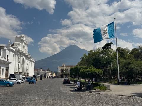 Guatemala’s blue-white flag waves over Antigua’s plaza with Volcán de Agua rising in the background.