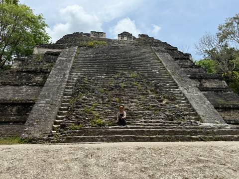 A lone visitor sits on the massive stone staircase of an ancient Maya pyramid in Tikal.