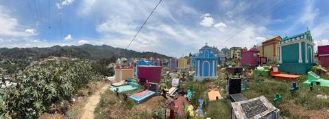 A colourful hillside cemetery features bright, multi-hued tombs beneath a wide Guatemalan sky.