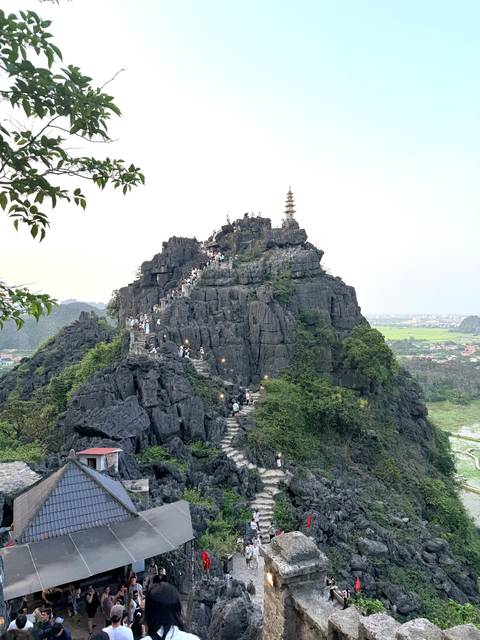 Steep stone stairway winding up a dark limestone peak crowded with visitors in Ninh Binh.