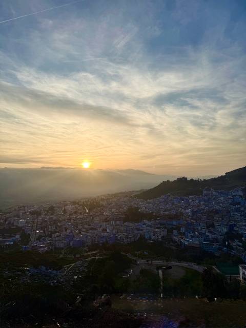Sun setting behind distant mountains, casting warm light over the blue-washed town below.