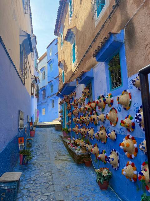 Narrow alley of bright blue buildings in Chefchaouen with colorful woven hats decorating the walls