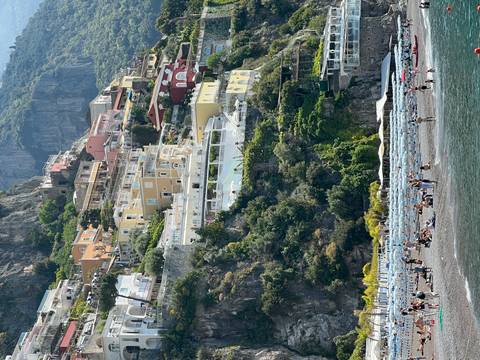 Vertical view of Positano’s colorful cliffside houses and busy beach with umbrellas.