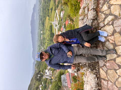 Older couple posing on stone viewpoint overlooking green valley and village.