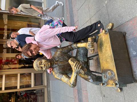 Woman playfully posing with bronze shoeshine statue on pedestrian street.