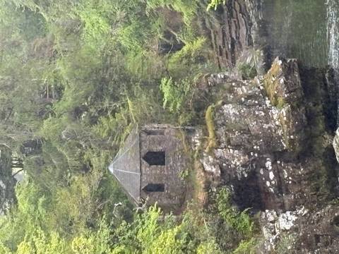 Small stone gazebo nestled on a mossy cliff in a lush Scottish forest.