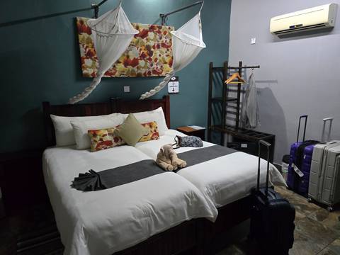Neat twin-bed lodge room with mosquito nets, suitcases and folded towel animal.