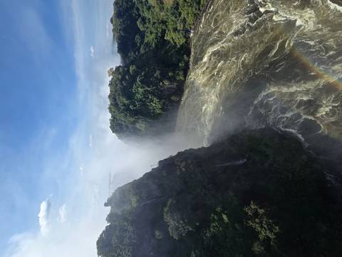 Powerful Victoria Falls with mist rising between lush cliffs and a faint rainbow below.