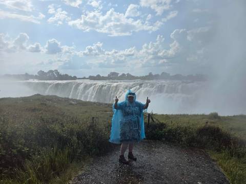 Traveller in blue rain poncho posing in front of mist-shrouded Victoria Falls.