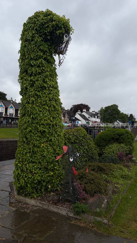 Small Scottish village canal lock area with ivy-covered trees, stone buildings and a few visitors walking along the waterway on an overcast day