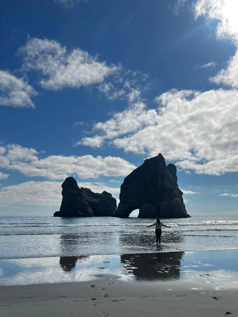 Dramatic twin sea stacks rising from calm ocean under bright blue sky with scattered clouds