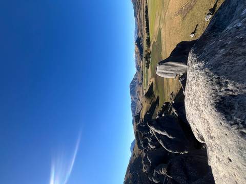 Rocky outcrop overlooking wide grassy plains and distant snow-dusted peaks beneath clear blue sky
