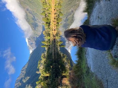 Traveller sitting by mirror-like lake reflecting snowy peak near Franz Josef Glacier