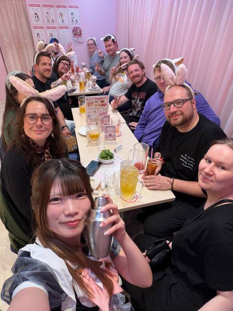 Friends gathered around a table of drinks and snacks in a brightly lit café.