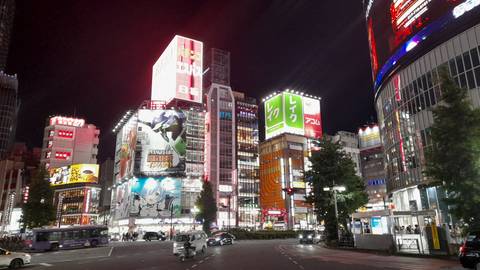 Vibrant night scene of Shibuya with neon billboards, busy traffic and illuminated buildings.