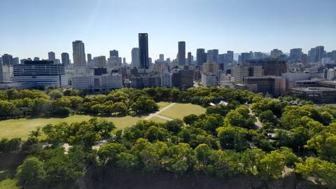 Panoramic city skyline of Osaka viewed over a lush green park from a high vantage point.
