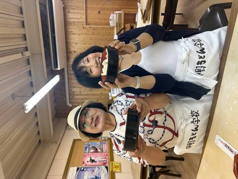 Two women in aprons proudly hold bowls of freshly made noodles during a Japanese cooking class.