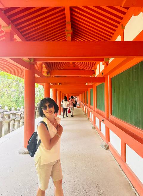 Smiling visitor stands in a long vermilion-painted corridor of a traditional Japanese shrine.