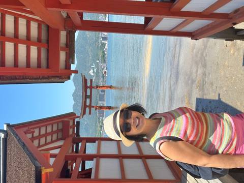 Traveller laughs beside the iconic floating torii gate of Itsukushima Shrine with mountains beyond the bay.