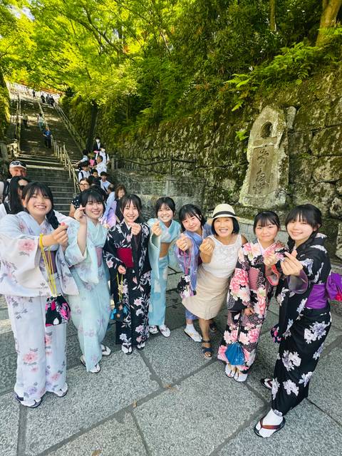 Tourist in hat poses with a group of local girls wearing colourful kimonos near stone temple steps.