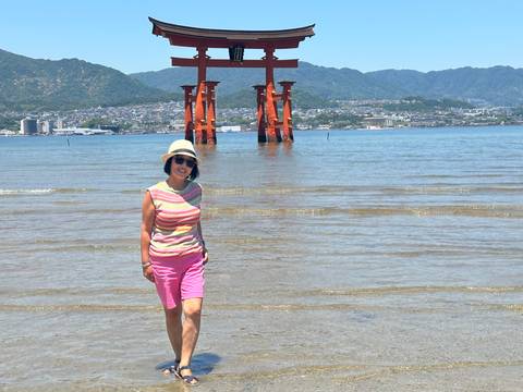 Traveller walks in shallow water near the majestic orange torii gate at low tide.