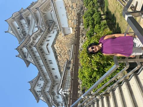 Visitor stands smiling in front of the imposing white towers and stone walls of Himeji Castle.