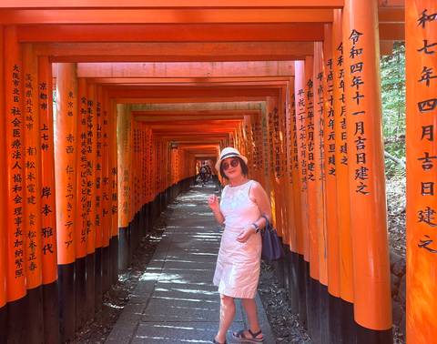 Woman poses mid-corridor inside the endless vermilion torii tunnels of Fushimi Inari Shrine.