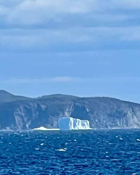 Distant iceberg floats against a backdrop of dark coastal cliffs under a blue sky.