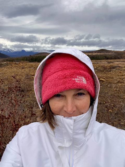 Close-up selfie of a bundled traveller with snowy mountains stretching across the horizon behind.