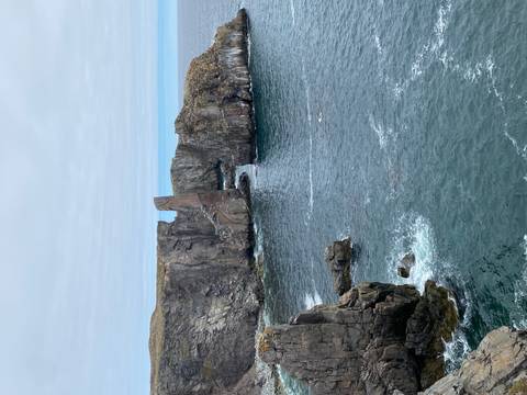 Rugged sea stacks and cliffs rise from churning Atlantic waters under a pale cloudy sky.