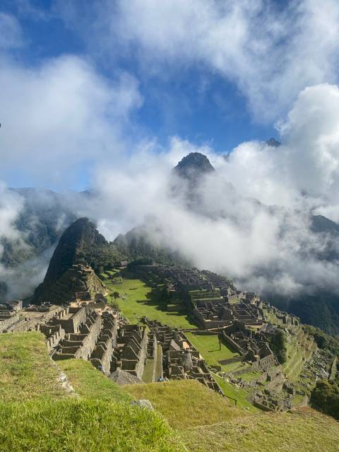 Iconic panoramic view of Machu Picchu ruins surrounded by lush green peaks and drifting clouds.