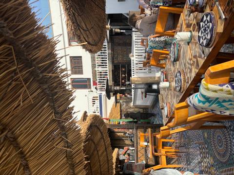 Open-air rooftop restaurant with wooden chairs, mosaic tile floor and straw canopies awaiting diners.