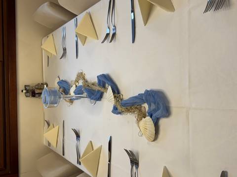 Elegant dining table on a ship set with folded napkins, cutlery and a seashell-and-net centerpiece.