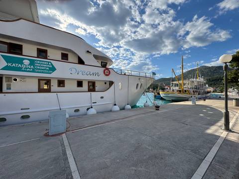 Docked white cruise vessel named Dream beside other boats in a sunny Croatian harbor bordered by wooded hills.