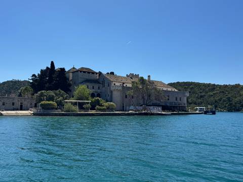 Historic stone monastery complex sits on a tiny forested islet surrounded by vivid turquoise water.