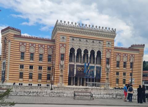 Striped Neo-Moorish Sarajevo City Hall with ornate arches and turrets under a partly cloudy sky.
