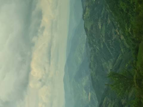Hazy panoramic view over layers of green mountains fading into mist under cloudy skies.