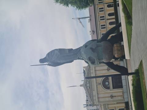 Modern monumental statue of a cloaked figure standing atop a globe outside a historic building.