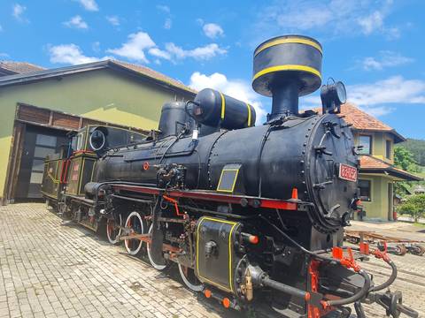 Restored black steam locomotive with red and yellow trim displayed outside a rural station on cobblestone track.