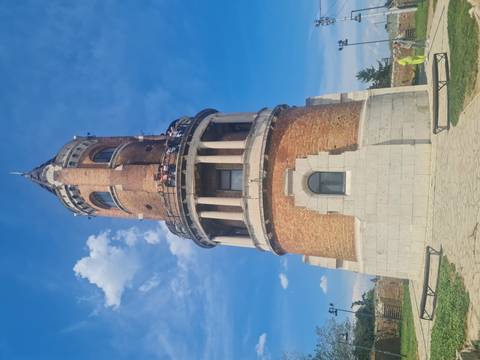 Brick Gardoš Tower with white stone base rises against blue sky as visitors look out from the balcony.